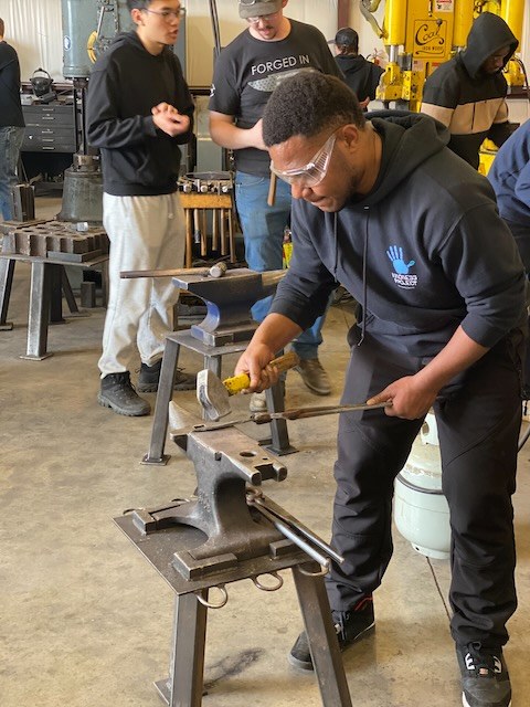 An adult student shaping metal with a hammer at an anvil in Kilroy's Workshop.