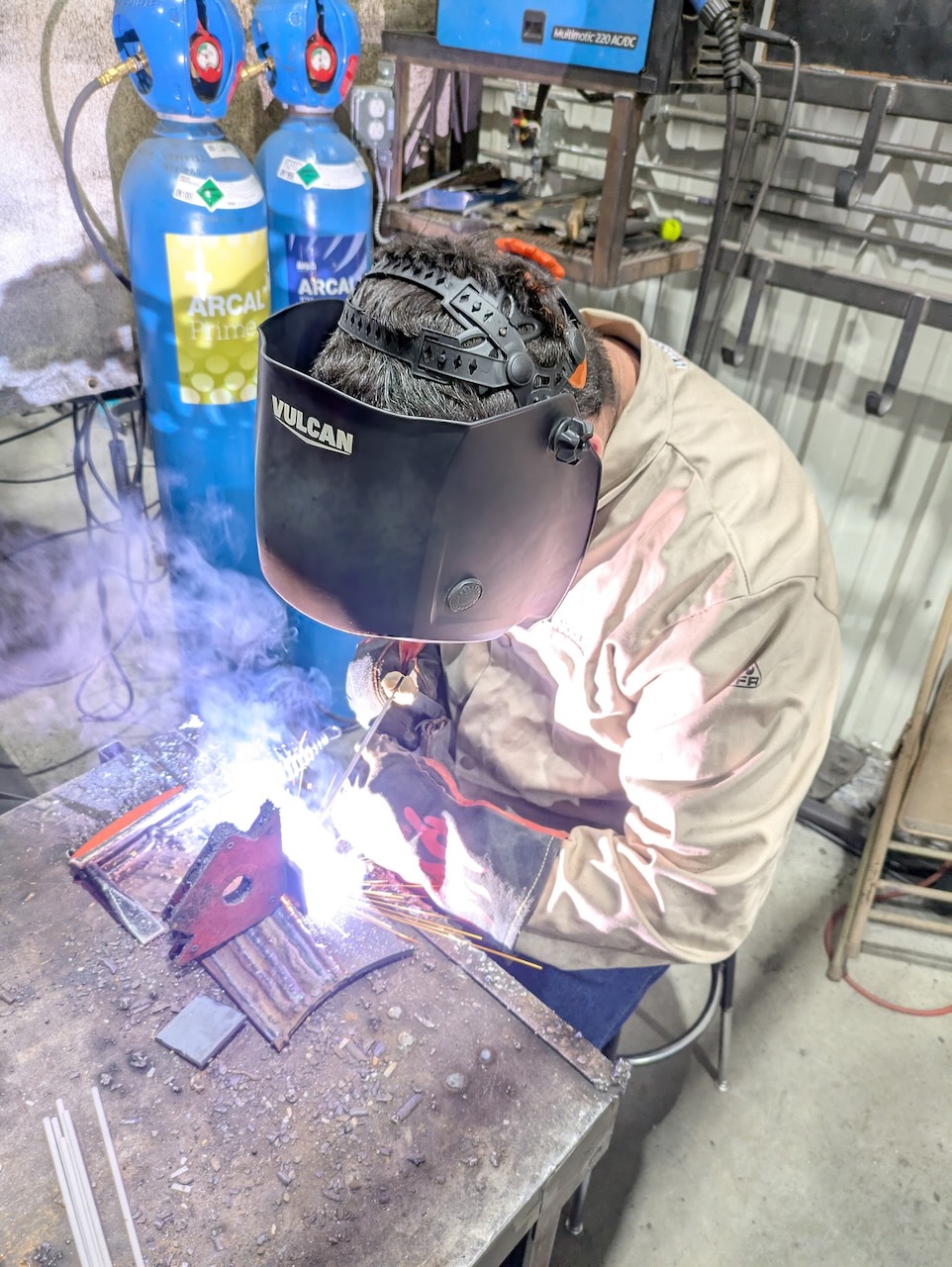 An adult welder wearing a protective helmet, jacket and gloves while welding a metal project at Kilroy’s Workshop.