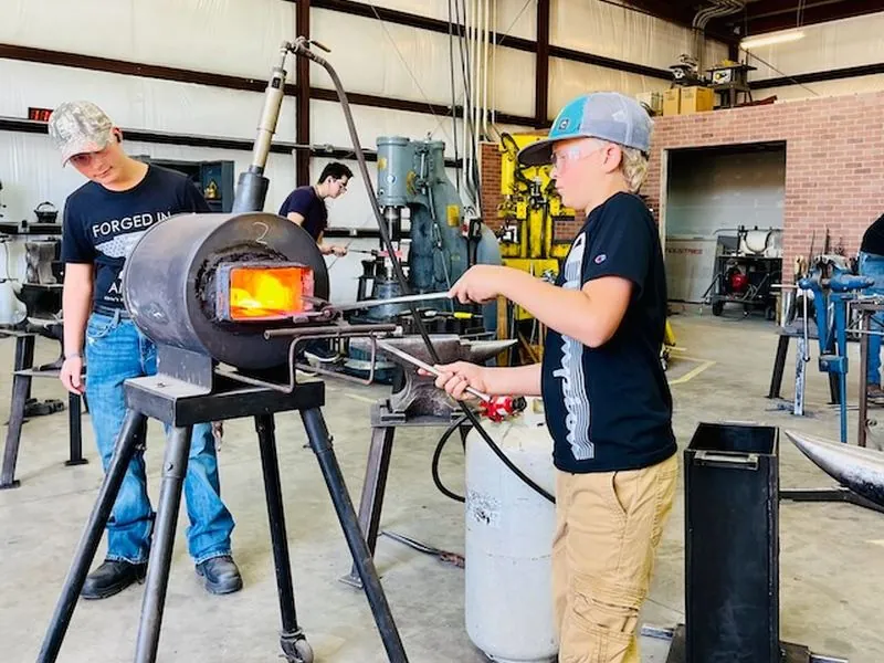 A young maker hammering glowing steel at the anvil.