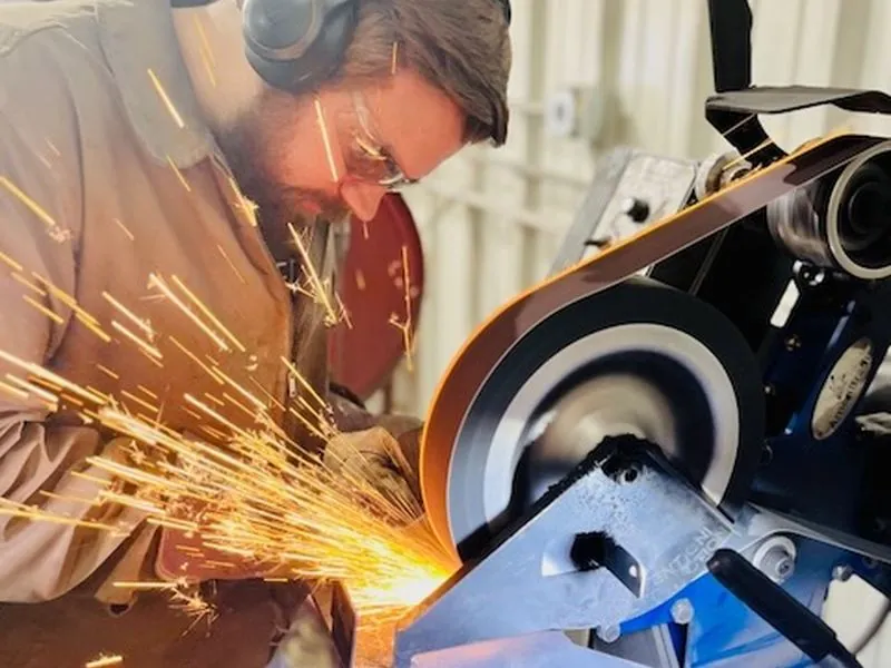 Grinding a blade on the belt grinder in a shower of sparks.