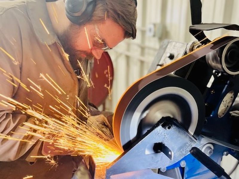 Grinding a blade on the belt grinder in a shower of sparks.