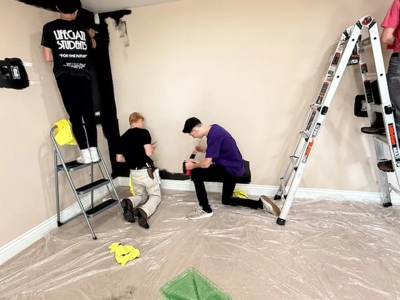 Students prepping and painting a room with ladders and drop cloths.