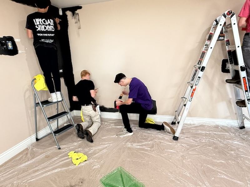 Students prepping and painting a room with ladders and drop cloths.