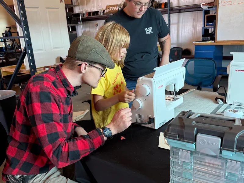 An instructor helping a young student thread a sewing machine.
