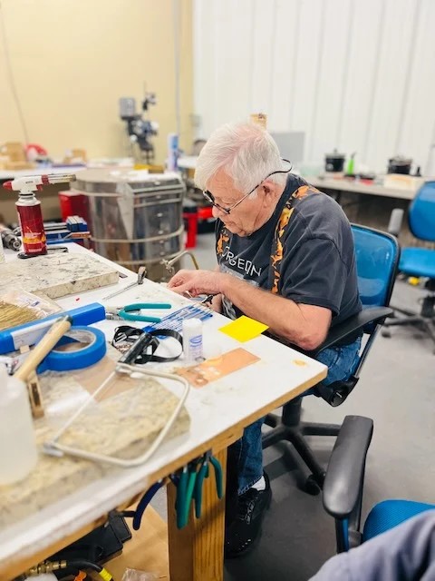 An adult maker in flame-pattern suspenders concentrating on a project at the workbench.