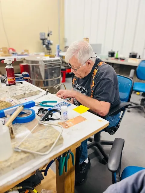 An adult maker in flame-pattern suspenders concentrating on a project at the workbench.